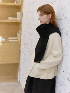Detail shot of a black knitted wool scarf worn by a model, showing the textured ribbed knit.