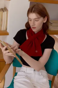 Detailed view of a cozy red winter neck warmer with cute floral embroidery, worn by a model reading.
