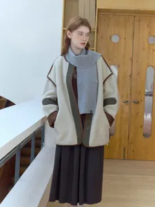 Detail view of stylish knit scarf and lamb wool coat outfit worn by model in bright indoor setting.