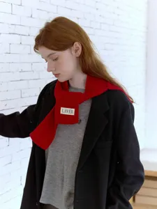 Dettaglio di sciarpa in maglia rossa con texture morbida e label per inverno.