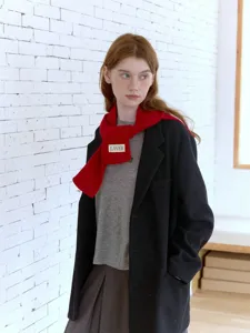 Dettaglio di una elegante sciarpa in maglia rossa su cappotto nero, moda invernale accogliente.