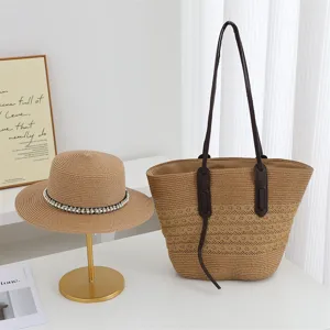 Detailed view of the woven straw tote bag and elegant sun hat on white table setup.