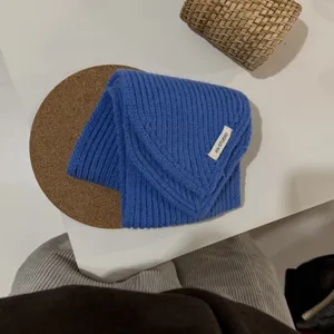 Detailaufnahme eines blauen Strick-Dreieckschals mit Rippmuster und Etikett auf dem Tisch.