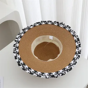 Close-up of a stylish wide-brim straw hat featuring black and white patterned fringe edge details.