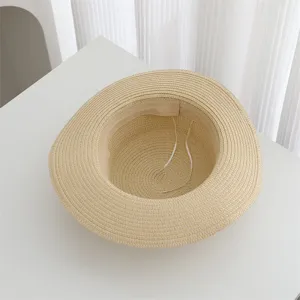 Close-up detail view of a minimalist beige woven straw sun hat on a white surface.