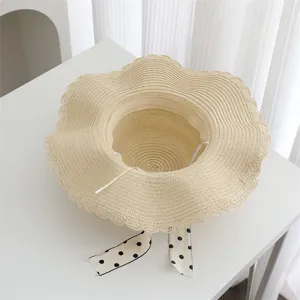 Detailed view of women's straw sun hat with wavy brim and polka dot ribbon for summer beach.