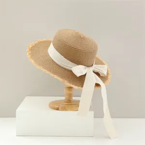 Foto de detalle de elegante sombrero de paja con ala deshilachada y cinta de lazo blanco.