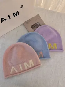 Soft wool knit beanie hat detail view featuring trendy letter design in pastel pink and blue.