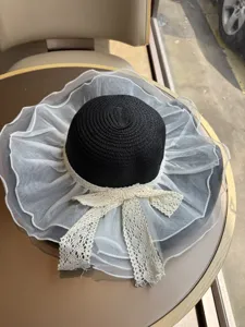 Eleganter schwarz-weißer Strohhut mit breiter Krempe und zarter weißer Mesh-Spitze.