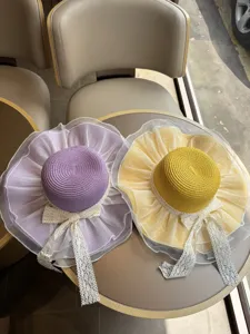 Nahaufnahme von breiten Strohhüten in Lila und Gelb mit zarten Spitzenschleifen Details.