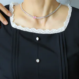 Gold tennis necklace detail with sparkling baguette zirconias and a chic central pink stone.