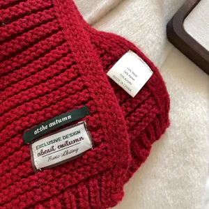 Close-up detail of red knitted wool blend scarf showing texture, brand tag and fabric label.