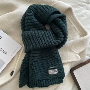 Detail view of the dark green knitted winter scarf showcasing soft texture and woven label design.