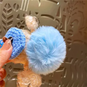 Detailopname van een schattige pluche poppensleutelhanger met blauwe pompon en gebreide muts.