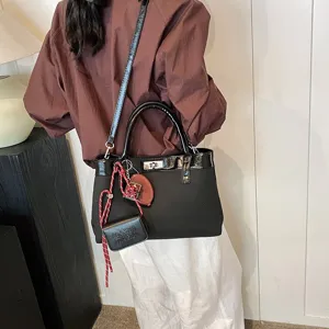 Women's stylish black shoulder bag with patent leather trim and chic charm accessories.