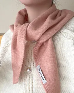 Close-up view of the soft wool-blend knitted triangular scarf detail in solid peach pink.