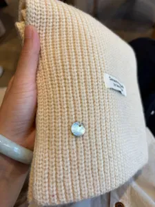 Cozy beige wool blend knit scarf with delicate shell pendant and handmade label detail for winter.