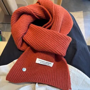Cozy orange knitted wool blend scarf with decorative shell button and woven label for winter warmth.