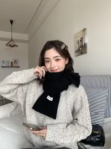 Detail view of a cozy black knitted scarf worn by an Asian woman in winter, soft and warm texture.