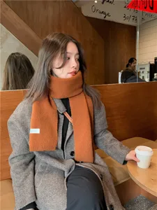 Detail view of a cozy caramel knit winter scarf worn by a model in a warm cafe setting.