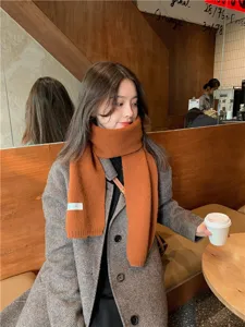 Close-up detail of a soft orange knit winter scarf worn in a cozy cafe scene.