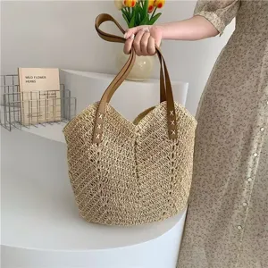 Vista dettagliata della borsa a mano in paglia intrecciata con manici marroni e trama.