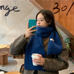 Detailed view of a cozy solid royal blue winter knit scarf worn in a warm cafe setting.