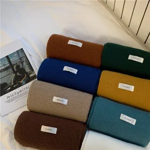 Detailed view of rolled winter knit scarves in assorted solid colors on a cozy white bed.