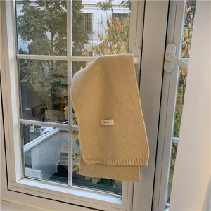 Close-up of a stylish yellow knit winter scarf hanging on a window handle with cozy indoor light.