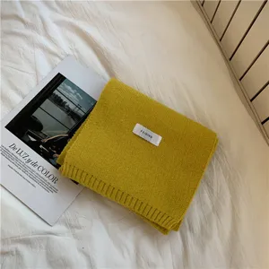 Detailed shot of mustard yellow knit scarf with fabric tag, cozy winter warm winter neck wrap.