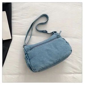Detail view of blue denim crossbody bag with adjustable strap and front zipper pocket detail.