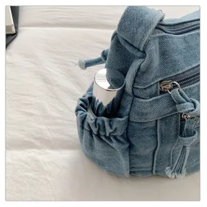Denim shoulder bag detail view showing side pocket, zipper, and vintage washed fabric texture.