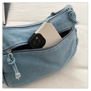 Blue denim shoulder bag detail featuring a convenient zippered front pocket and knot strap.