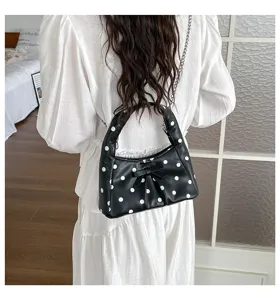 Details of the stylish black polka dot underarm bag featuring a cute bow and chic chain strap.