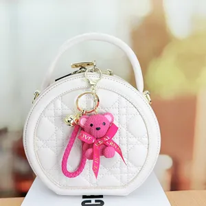 White quilted round handbag featuring a cute pink woven bear keychain pendant for women.