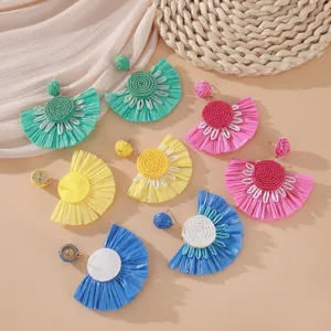 Dettaglio ravvicinato di orecchini a fiore con nappe di rafia in vari colori vivaci.