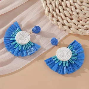 Dettaglio di orecchini a ventaglio in rafia blu con perline bianche per stile vacanza.