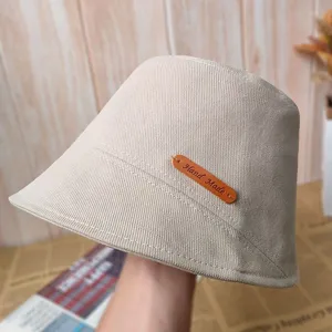 Détail de chapeau bob beige montrant l'étiquette en cuir faite main et le tissu texturé.