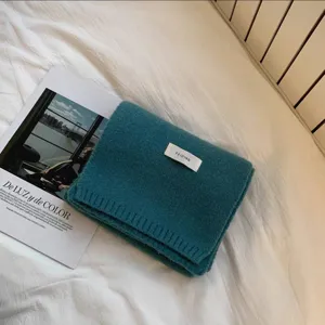 Primo piano di una sciarpa invernale in maglia verde scura, piegata ordinatamente sul letto.