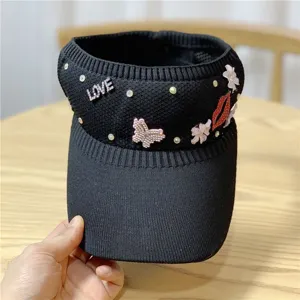 Cappello con visiera parasole nero lavorato a maglia con strass e decorazioni a labbra.