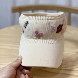 Cappello visiera in maglia beige con strass farfalla e simpatici dettagli labbra.