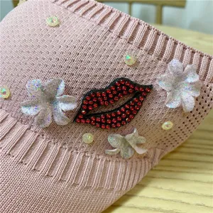 Primo piano della visiera rosa in maglia con labbra di strass lucide e decorazioni floreali.