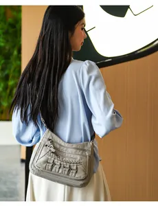 Detail shot of a grey multi-zipper soft leather shoulder bag worn by a model indoors.