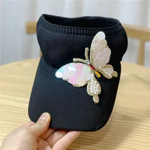 Primo piano del cappello da sole nero in maglia con farfalla di paillettes scintillanti.