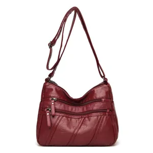 Womens wine red soft leather cross body shoulder bag with multiple zippers and adjustable strap.