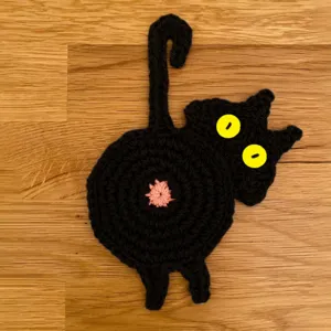 Gros plan d'un drôle de sous-verre chat noir au crochet, joli détail de tapis de table.