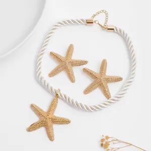 Makroaufnahme eines goldenen Seestern-Schmucksets mit weißer Seilkette und passenden Ohrringen