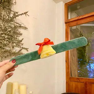 Gros plan du détail du bracelet slap en peluche de Noël avec cloche jaune et nœud rouge.