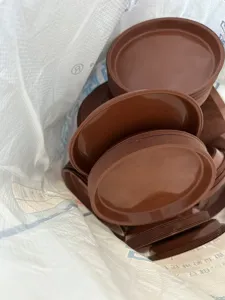 Detail view of stacked brown plastic plant saucer trays inside a large packaging bag.