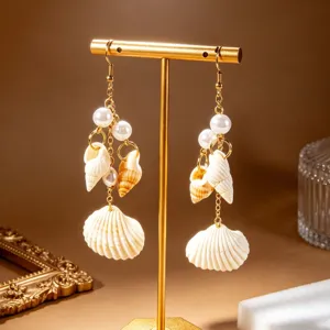 Detalle de los pendientes colgantes de conchas y perlas de estilo playa en soporte dorado.